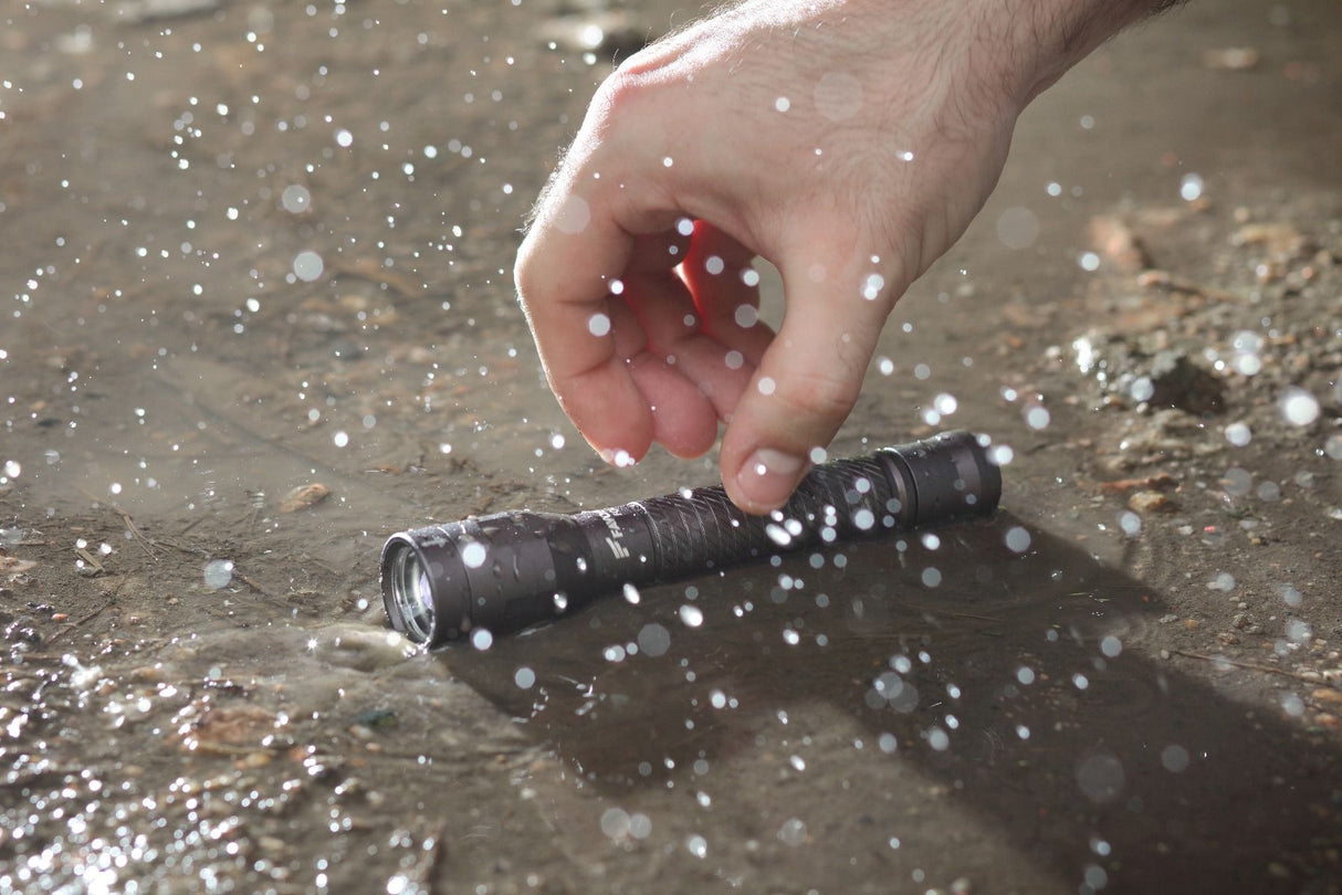 Favour T1921 zaklamp liggend in het zand in regenachtige omgeving die opgepakt wordt