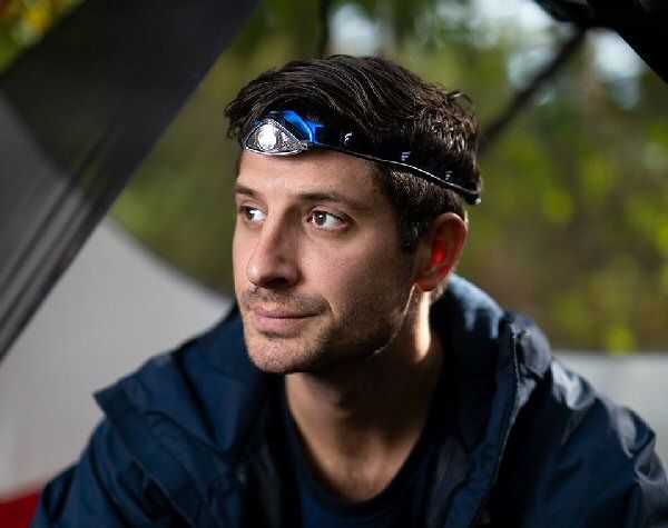 Man in een tent die de Favour H1311 hoofdlamp draagt. Deze is voorzien van 55 lumen witte leds aan de voorzijde en rode leds aan de achterzijde