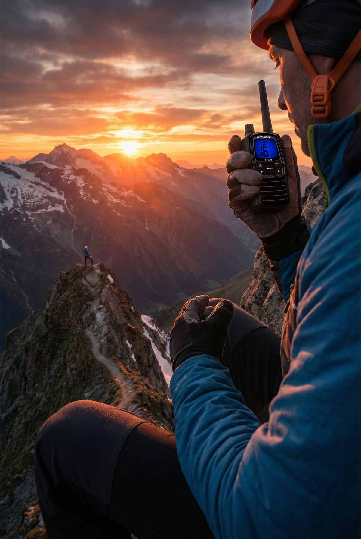 Bergbeklimmer met een Midland G7 EVO portofoon in de hand aan het communiceren is met uitzicht op zonsondergang achter de bergen