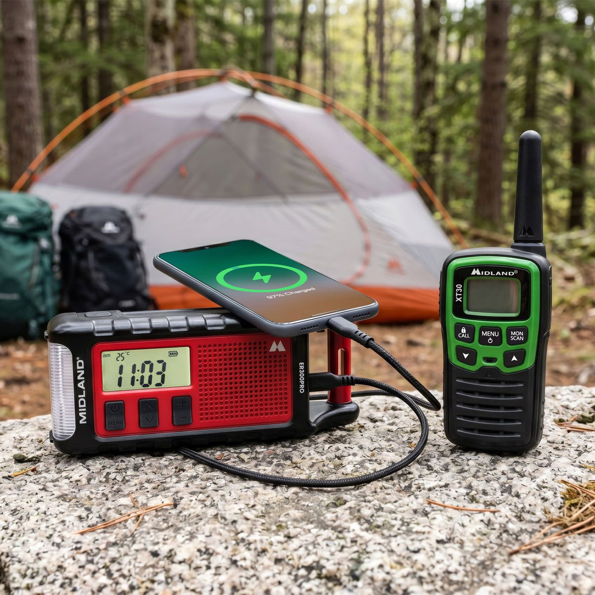 Midland ER300 Pro noodradio waaraan een mobiele telefoon wordt opgeladen op een kampeerplaats in het bos