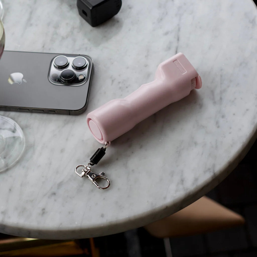 Roze Plegium zelfverdedigingsspray naast een Apple iPhone op een tafeltje