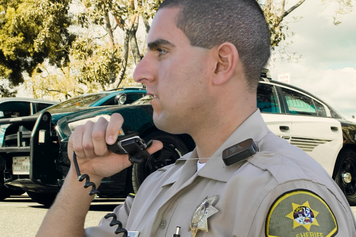 Politie agent die praat door een handmicrofoon die bevestigd zit aan een Gear Keeper lapel microfoon retractor