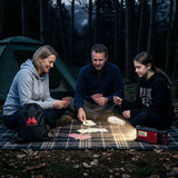 Man, vrouw en dochter die in de schemering bij de tent op een kleed zitten te kaarten en de Midland ER300 gebruiken als verlichting
